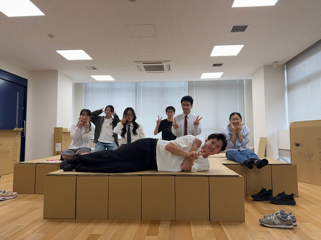 段ボールベッドの上でポーズをとる訓練参加者たち